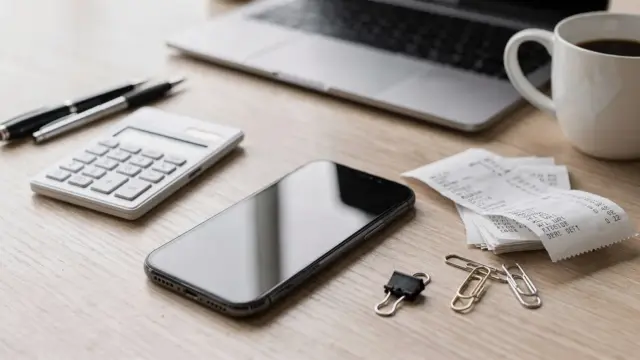 Smartphone neben Belegen und Taschenrechner: Thema sind versteckte Zusatzkosten bei einer Steuer-App.